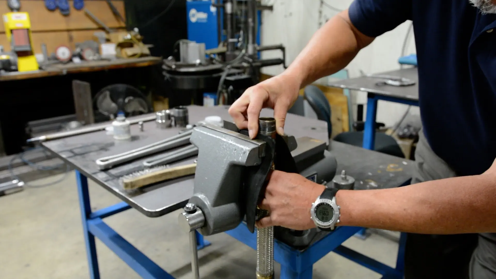 Leak tester inserts rubber-pad-wrapped small diameter metal hose into a vise to prepare its NPT ends for leak testing. The rubber pad will protect the braid from damage.
